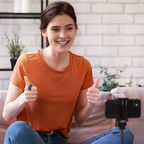 Person sitting on a couch giving a thumbs-up in a home setting with a smartphone on a tripod.